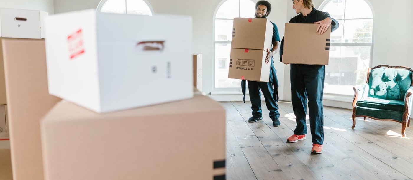 Zwei Umzugshelfer tragen Umzugskartons in eine helle, leere Altbauwohnung