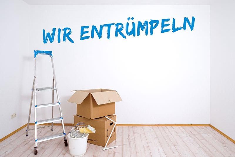 Leergeräumter Raum mit Leiter und Umzugskartons und dem Schriftzug "Wir entrümpeln" an der Wand